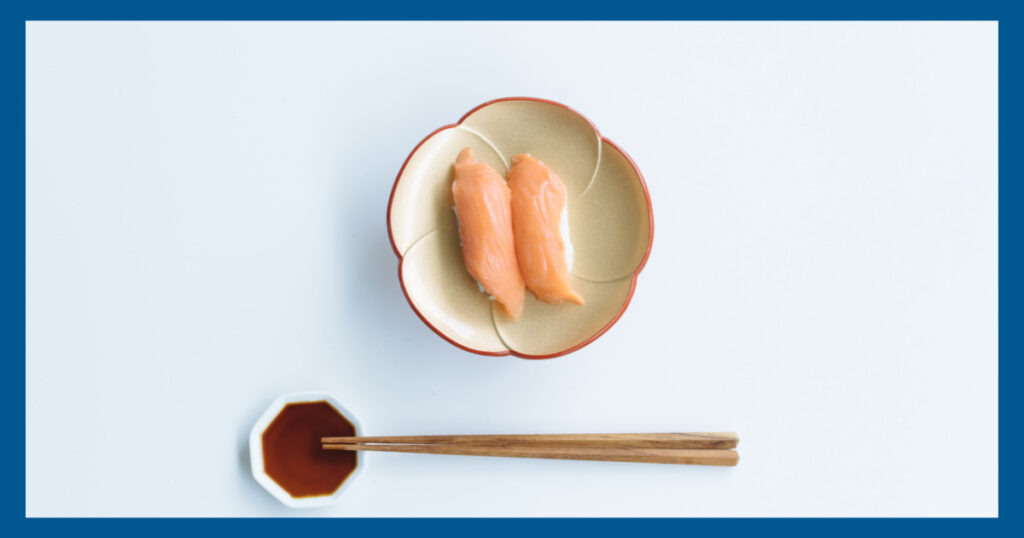 和の紺の枠に、お寿司一貫とお箸とお醤油が入った小皿の画像